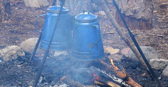 Pots of coffee brewing over a campfire.